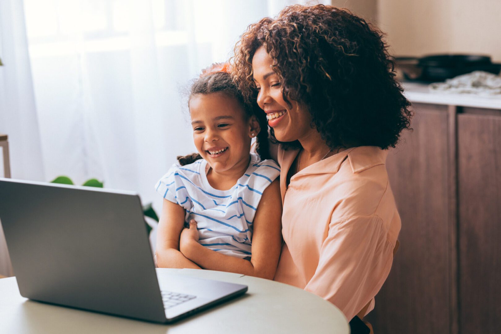 Mother and daughter smiling at laptop screen.
