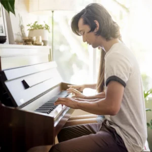 Man playing piano in a sunlit room.