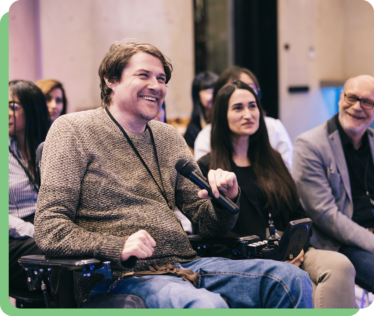 Man in wheelchair smiling, holding microphone.