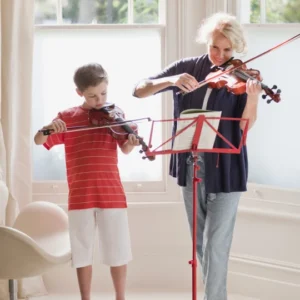 Two people playing violins by window.