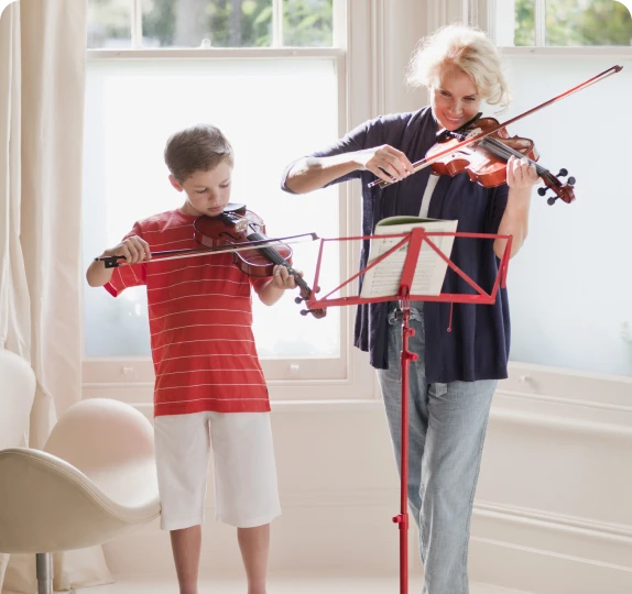 Two people playing violins by window.